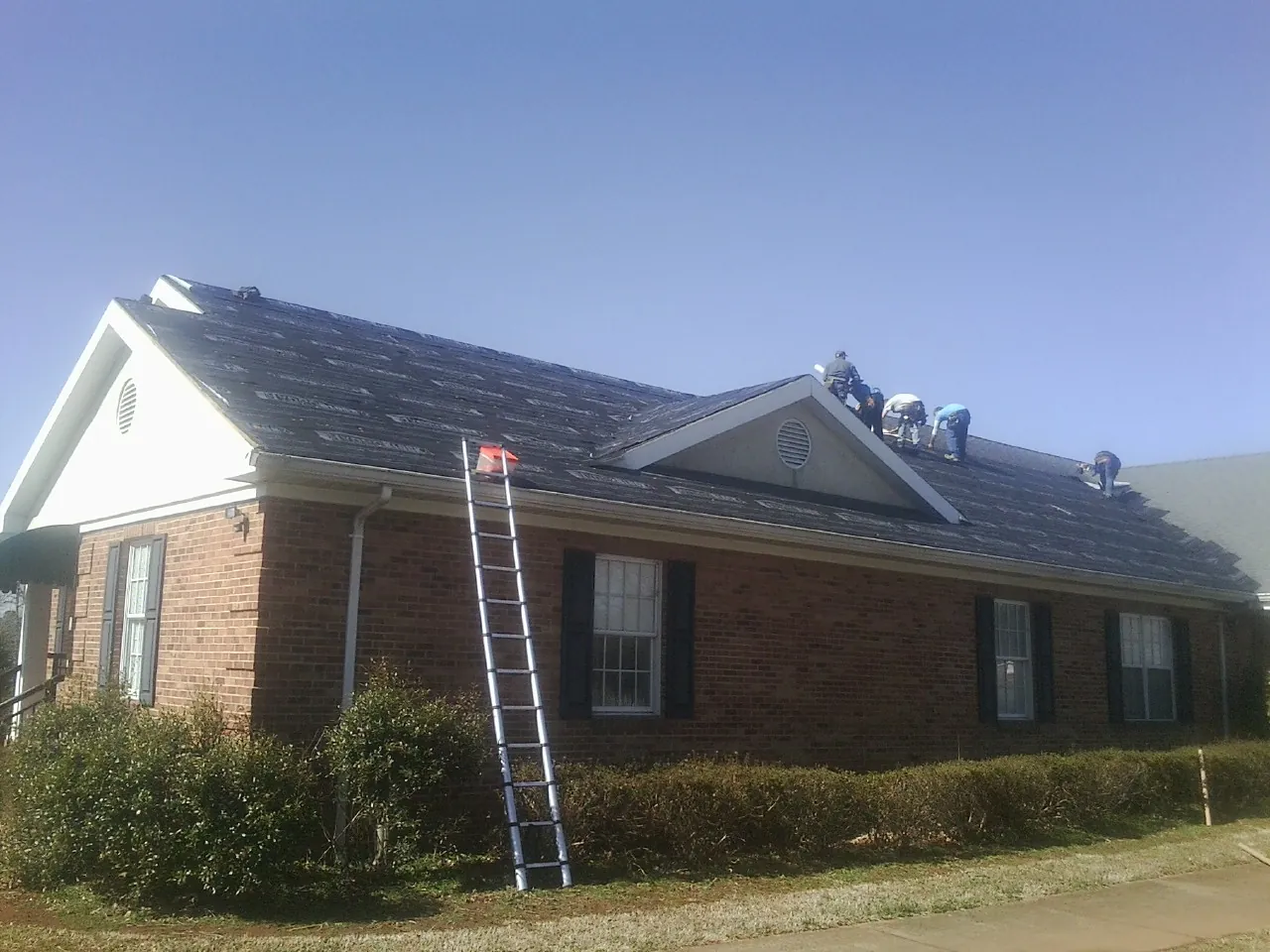 Crew tearing shingles off a brick ranch roof with a ladder set — Emergency Roof Repair work by our crew in Nunica
