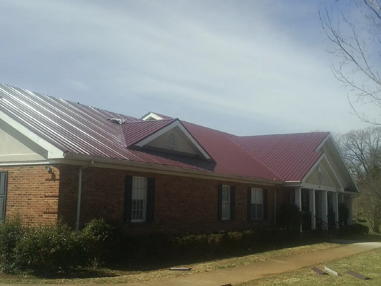 Red metal roof with gabled entries on a long brick building, from a Hail Damage Roof Repair job in Nunica