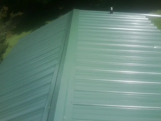 New green metal panels meeting at the ridge of a roof — Flat Roof Repair work by our crew in Nunica