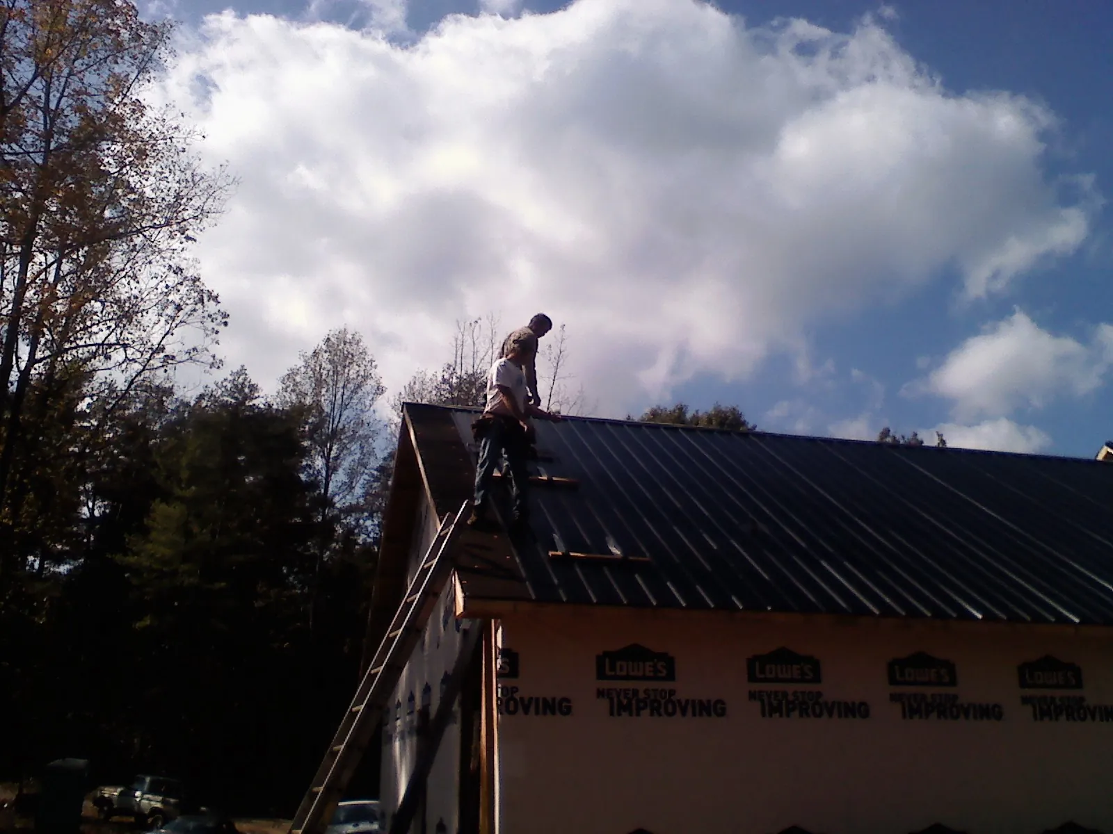 Roofer fastening dark metal panels high against a cloudy sky, from a Roof Inspection job in Nunica