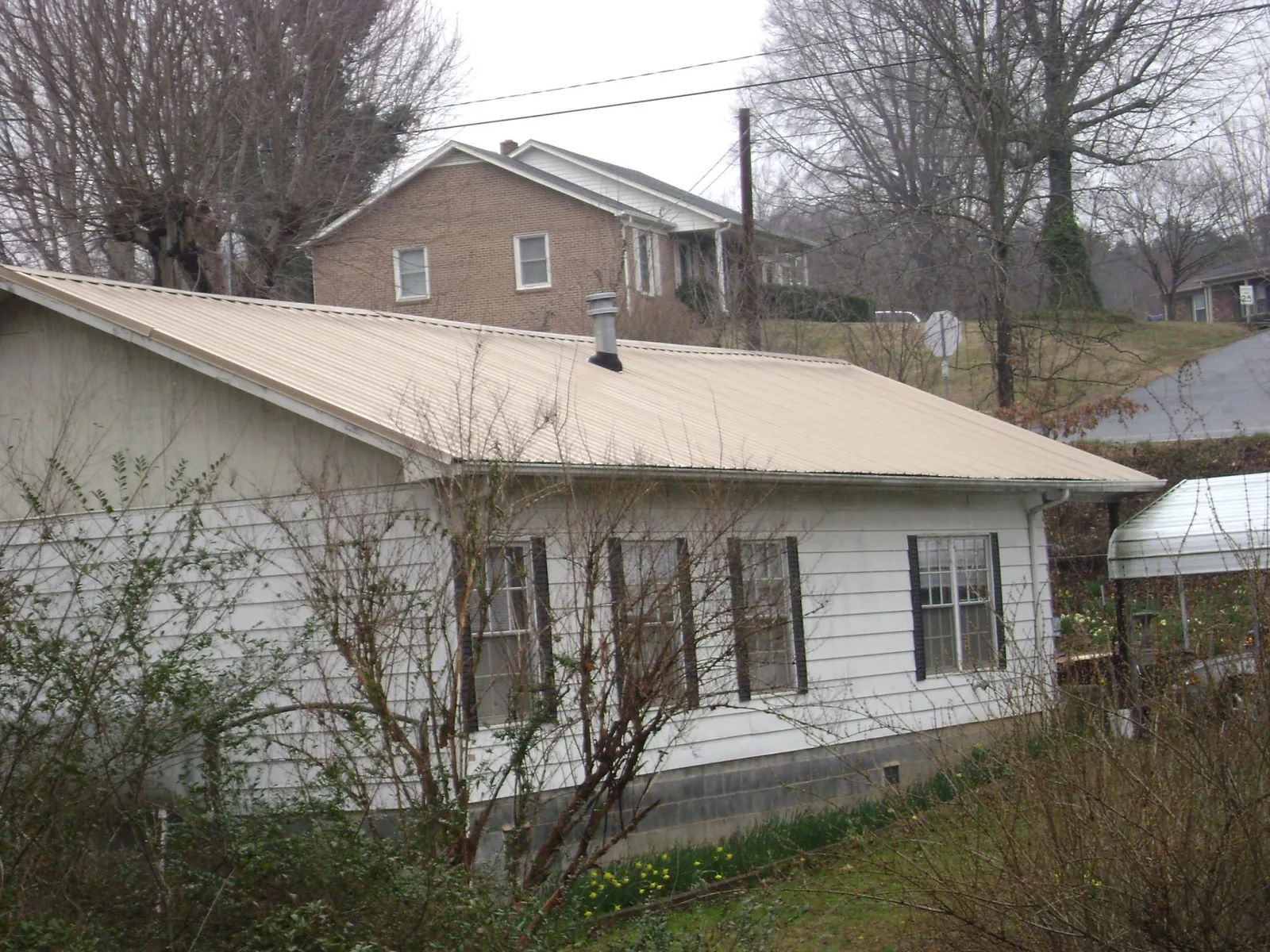 Tan metal roof on a white sided house set into a hillside — Commercial Roofing by Roofing Brothers in Nunica
